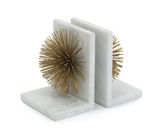 Two white marble bookends shaped like starburst, with a gold metal sculpture on top. The sculpture is detailed and intricate, and the bookends have a smooth, polished finish.