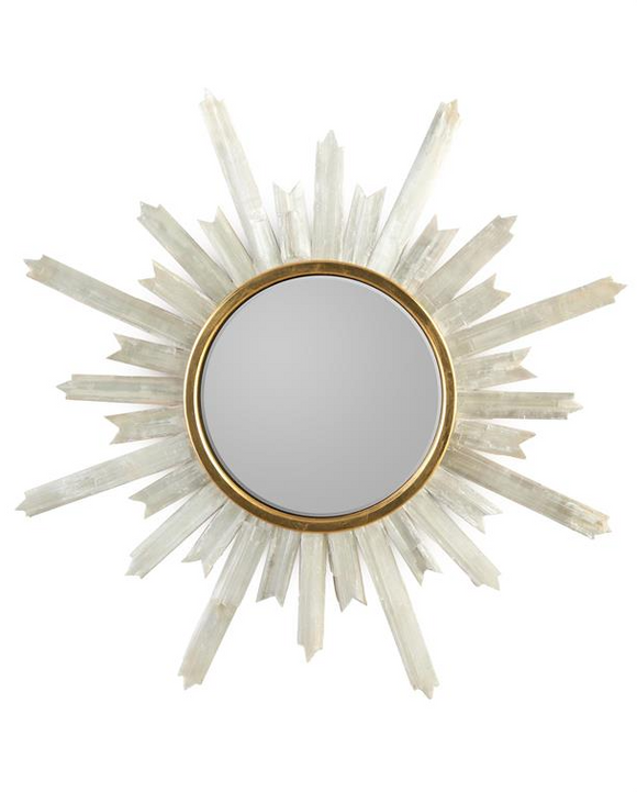 A round mirror with a gold metal sunburst frame, hanging on a white wall. The sunburst frame has long, pointed rays that extend outwards from the center of the mirror.